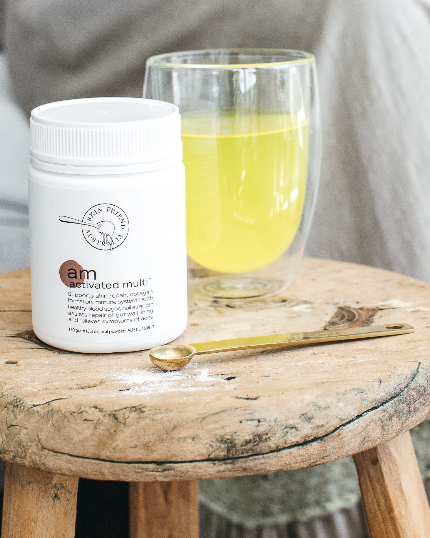White container labeled 'am Activated Multi' on a wooden stool with a glass of yellow liquid.