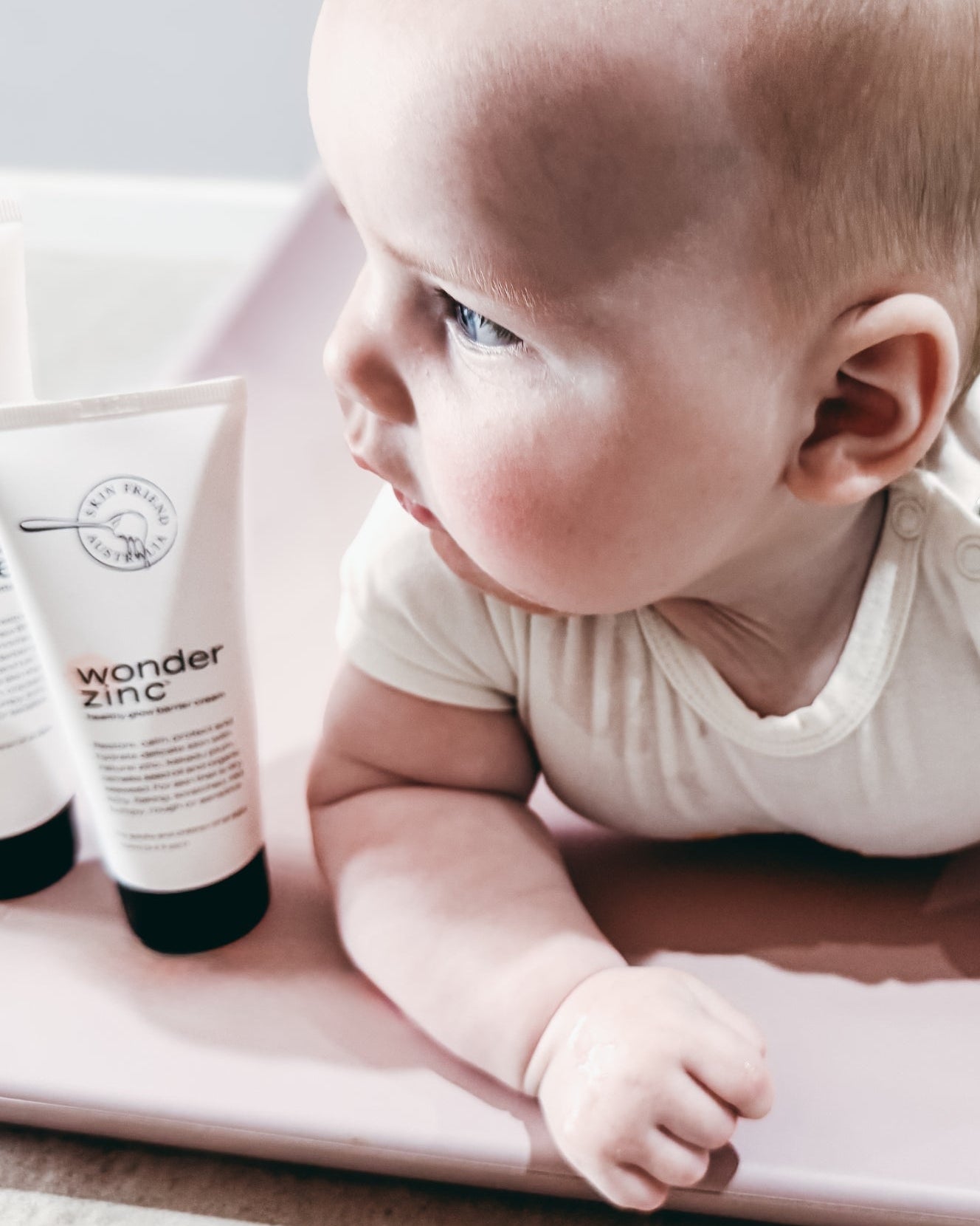 Baby lying on a pink blanket next to a tube of 'wonder zinc' cream.